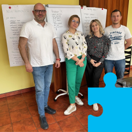 Na tle flipchartów stoją dwaj mężczyźni (po bokach) i dwie kobiety (w środku).