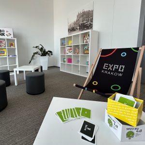 Wnętrze pokoju, w którym stoją regały z książkami, stoliki z grami planszowymi, leżaki i pufy.