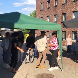 Grupa ludzi tańczy na dziedzińcu pod gazebo.