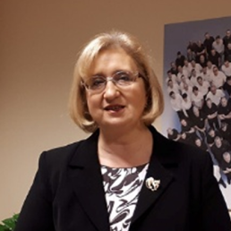 Blondynka w okularach z włosami do ramion, w czarnym żakiecie z broszką