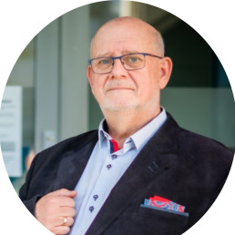 Mężczyzna w średnim wieku, w okularach, błękitnej koszuli i ciemnej marynarce z kolorową poszetką