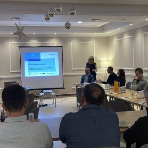 Grupa ludzi siedzi na sali konferencyjnej, patrząc na ekran z prezentacją pod tytułem: "Biznes zaczyna się od ludzi".