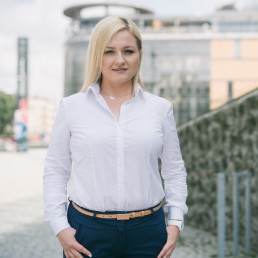Blondynka w białej koszuli, w tle rozmyte budynki