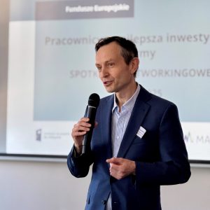 Mężczyzna w średnim wieku w granatowej marynarce mówi do mikrofonu.