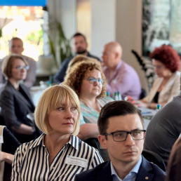 Zbliżenia na twarze kobiet i mężczyzn siedzących na spotkaniu.