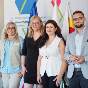 Trzy kobiety i mężczyzna stoją razem, uśmiechając się do kamery.