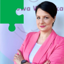 Młoda kobieta z krótkimi czarnymi włosami uśmiecha się do kamery z rękami założonymi na piersi.