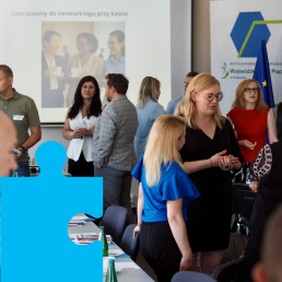 Elegancko ubrani ludzie stoją w sali konferencyjnej i rozmawiają ze sobą w grupach.