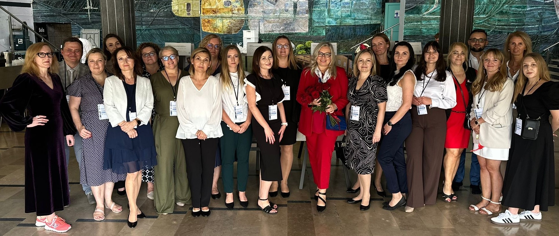 Grupa elegancko ubranych kobiet i mężczyzn uśmiecha się, patrząc w obiektyw aparatu fotograficznego.