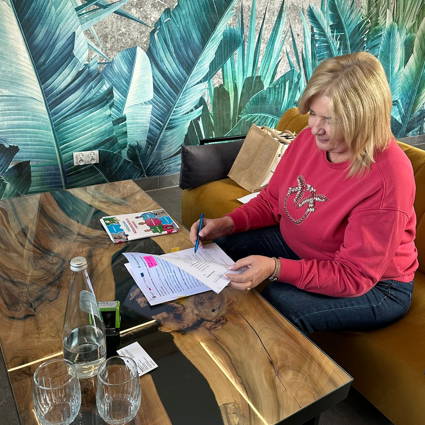 Blondynka w średnim wieku podpisuje dokumenty przy stole.