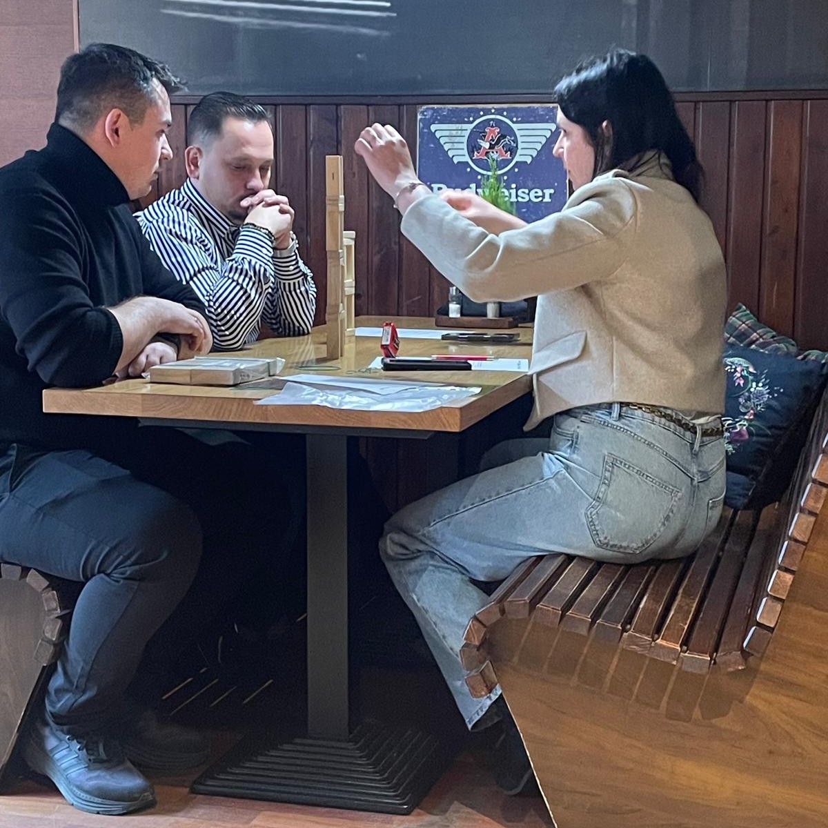 Dwóch mężczyzn i kobieta budują wieżę z klocków.