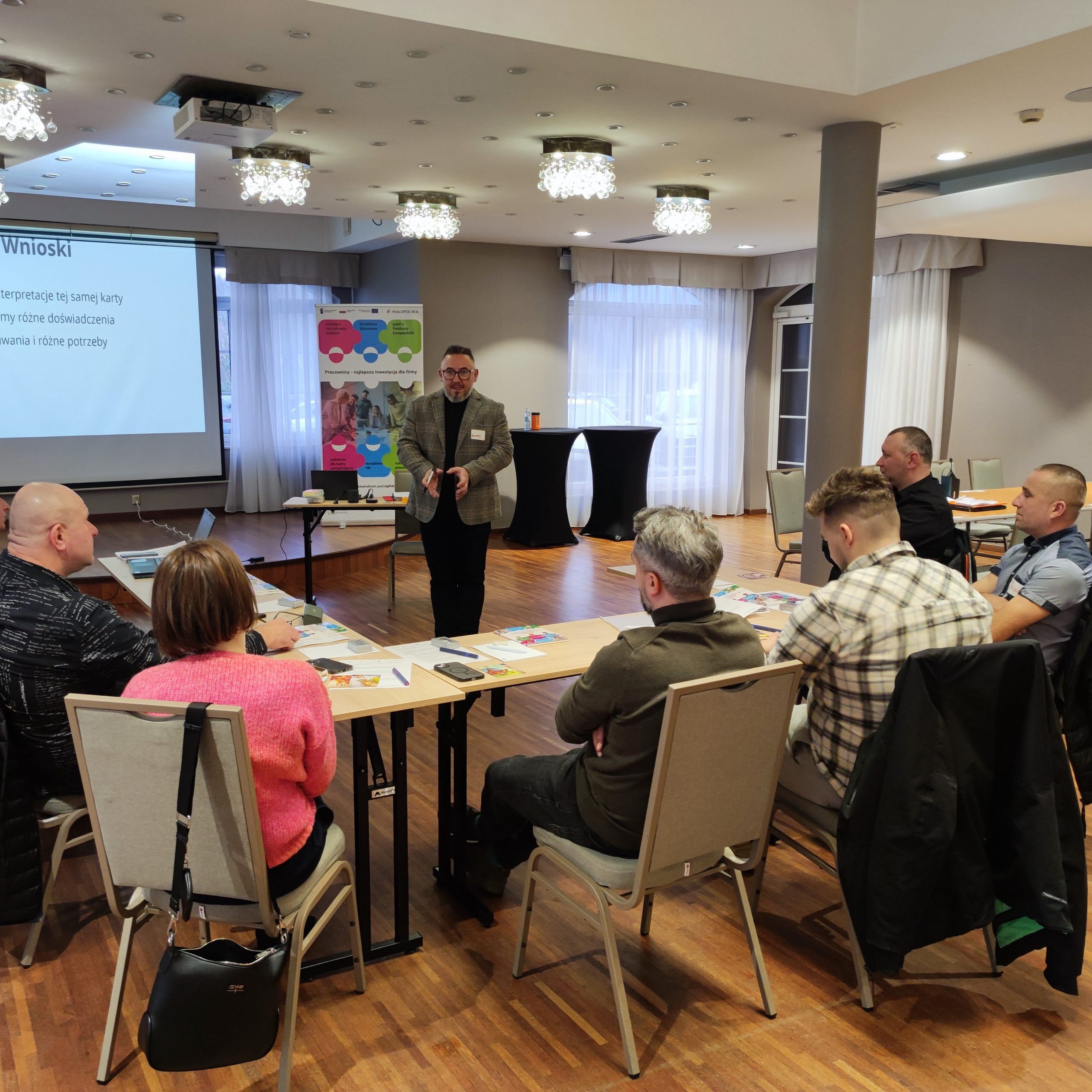 Trener - mężczyzna w średnim wieku w okularach mówi do grupy na szkoleniu.