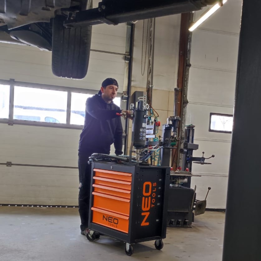 Młody mężczyzna pcha wózek z narzędziami w warsztacie samochodowym.