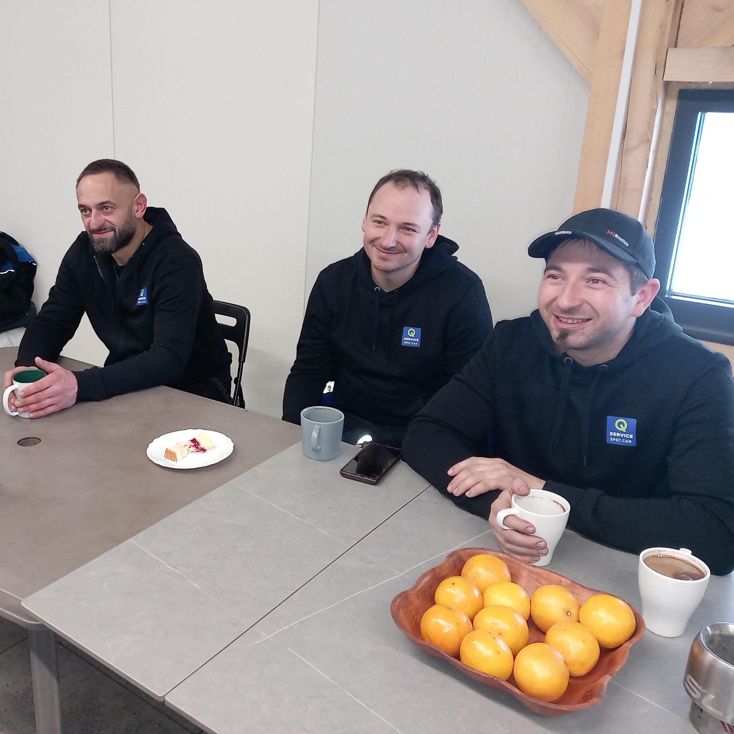 Trzech mężczyzn siedzi przy stole z kubkami kawy w rękach.