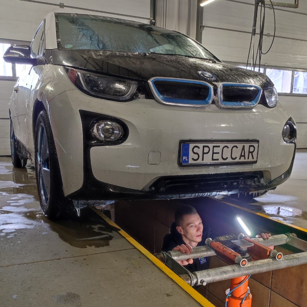 Młody mężczyzna, stojący w kanale, pracuje pod samochodem.