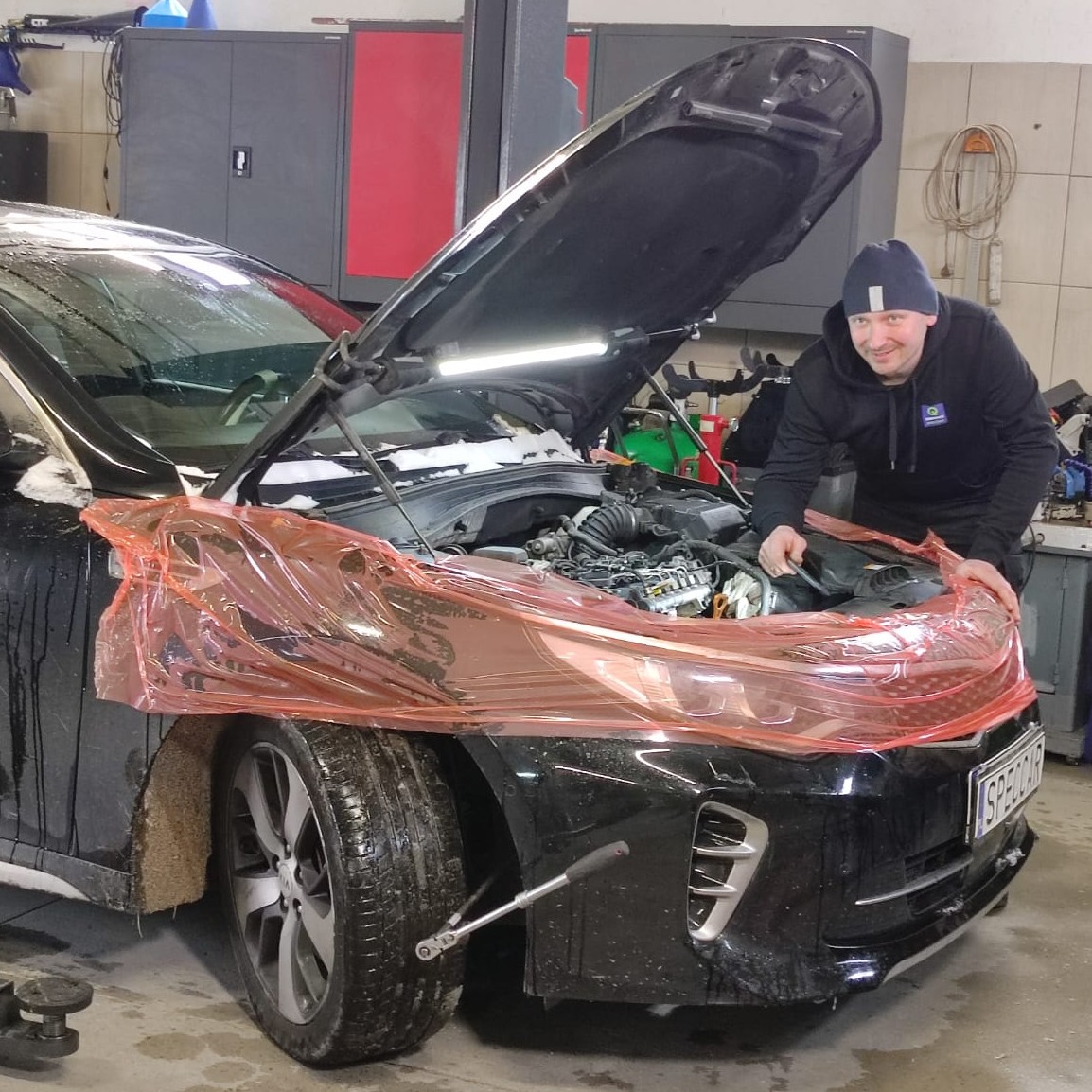 Młody mężczyzna pracuje przy otwartej masce samochodu.