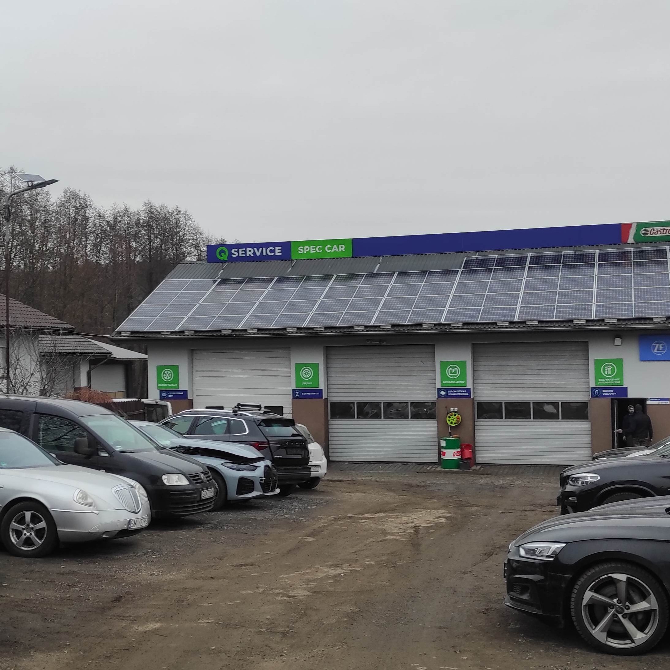 Na placu przed warsztatem samochodowym stoją samochody.