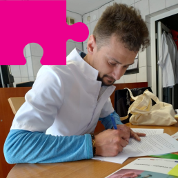 Młody mężczyzna w białym kitlu pochyla się nad stołem i podpisuje dokumenty.